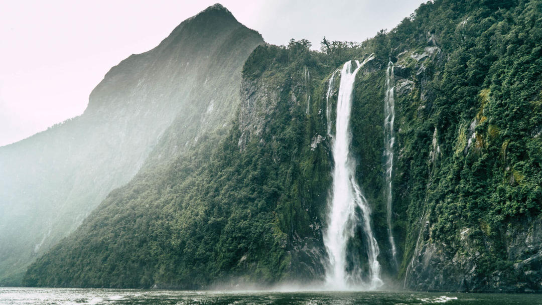 a large waterfall over a body of water with a mountain in the background